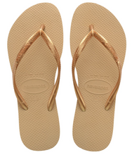 Load image into Gallery viewer, A pair of gold Havaianas flip-flops with shiny textured metallic straps, prominent Havaianas logo embossed on the footbed, and a signature rice grain pattern
