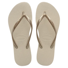 Load image into Gallery viewer, Digital photograph, Havaianas, of a pair of beige textured flip-flops featuring slim metallic gold straps and embossed brand name