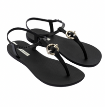 Load image into Gallery viewer, A pair of black flat sandals with ankle straps and decorative metal rings on the thongs.
